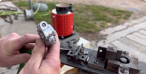Hand holding a small cast metal part beside an electric melting furnace and metal mold fixture